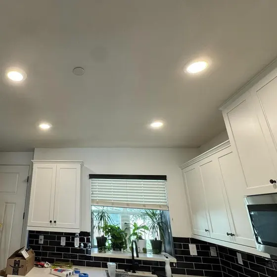 A kitchen with white cabinets and black tiles and a window.