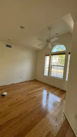 An empty room with hardwood floors and a ceiling fan.