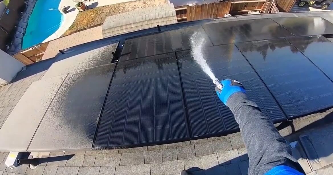 A person is cleaning a solar panel on the roof of a house.